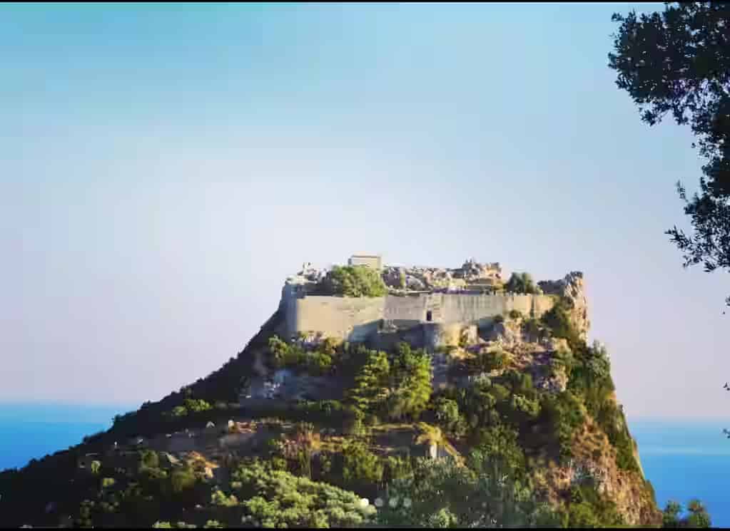 The Byzantine castle of Angelokastro perched on a steep, lush green cliff overlooking the Ionian Sea, a must-visit panoramic viewpoint for travelers with a Corfu car rental.