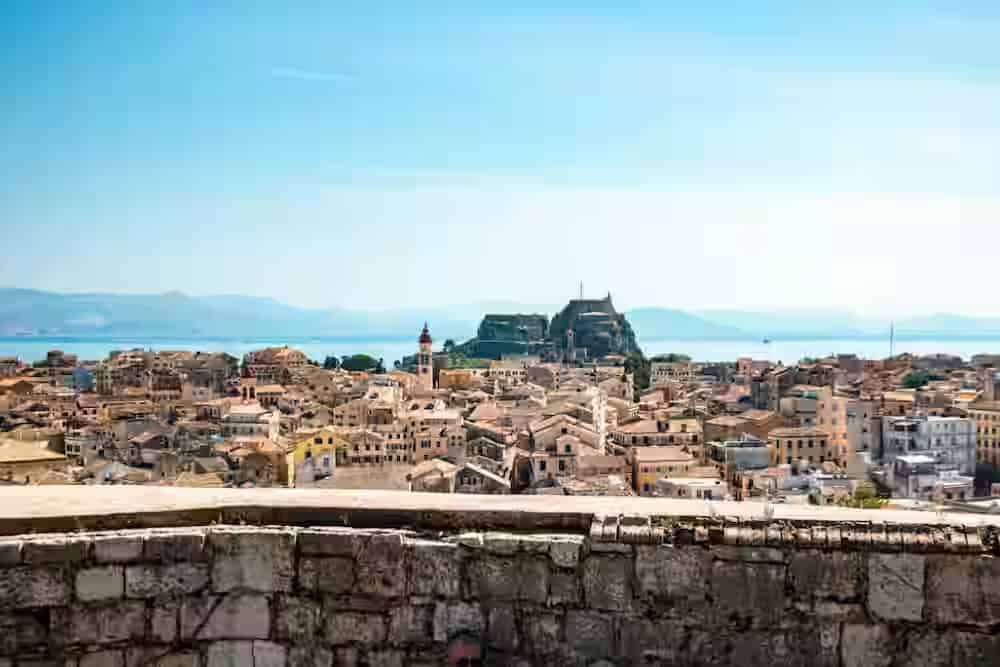 Panoramic view of the historic Corfu Old Town with its orange-tiled rooftops and the Venetian Old Fortress by the Ionian sea, a key destination for travelers renting a car.