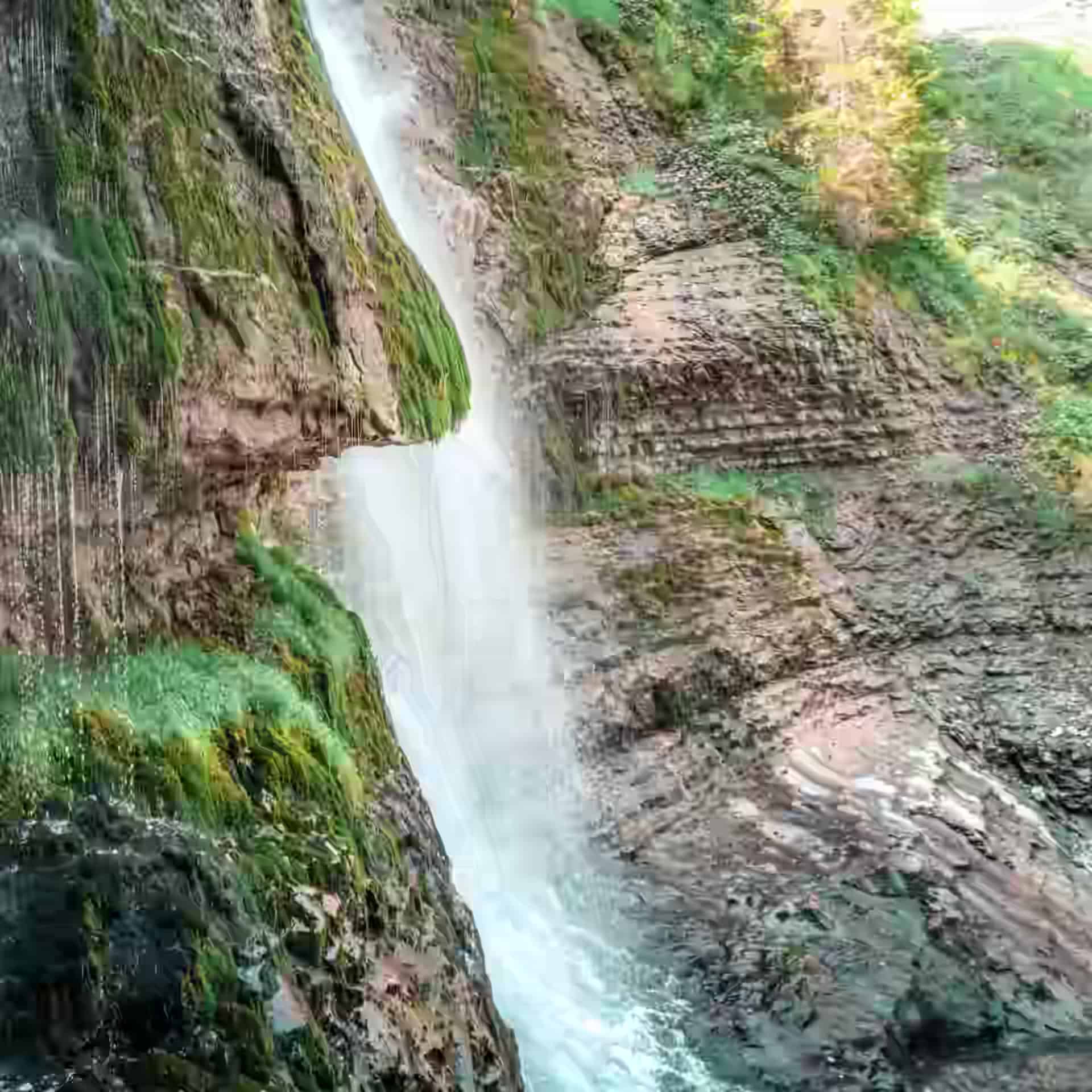 Ein Wasserfall stürzt an geschichtetem, bemoostem Fels vorbei bei den Mirusha-Wasserfällen.
