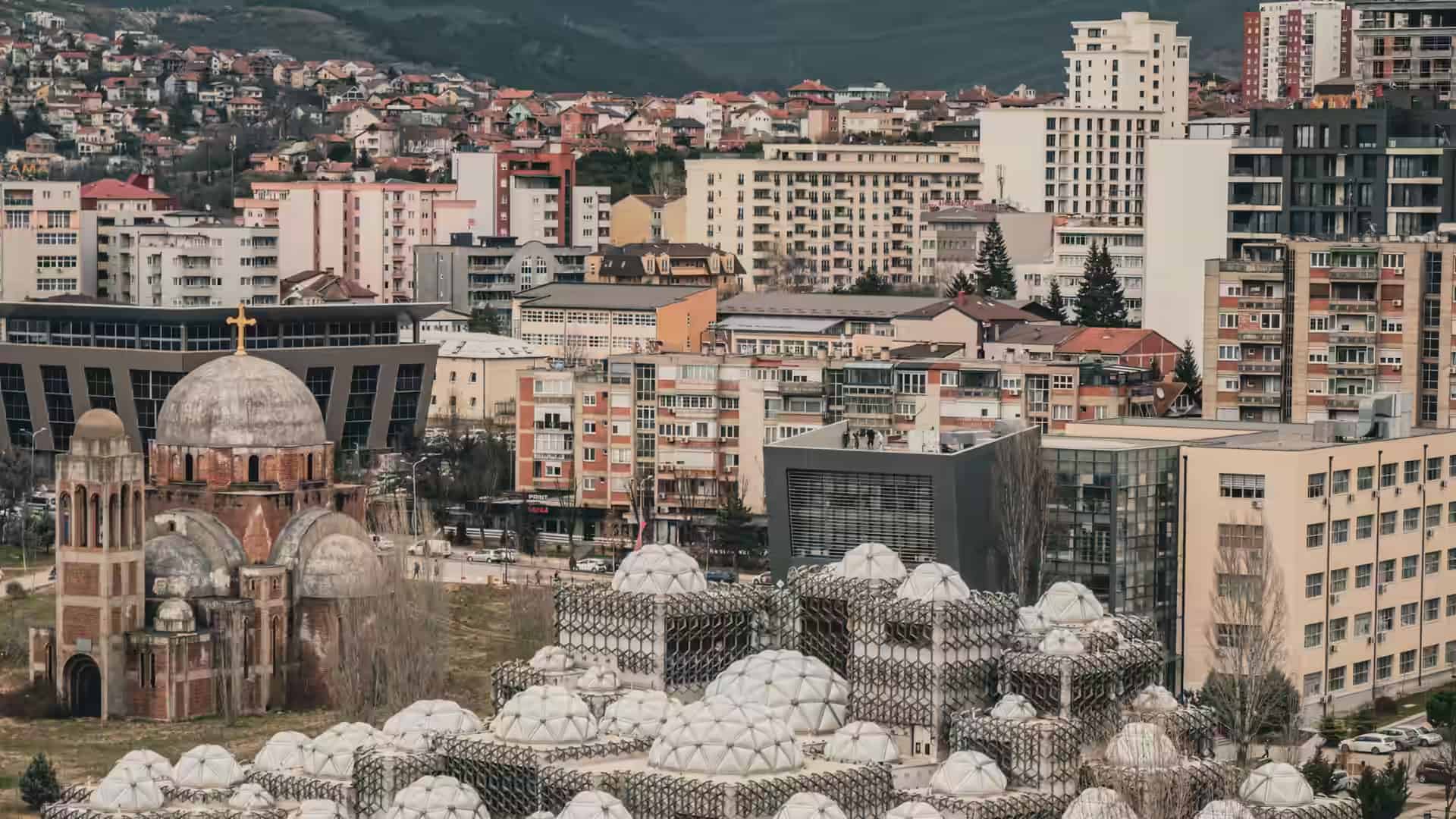 Bloques de viviendas de Pristina tras la Biblioteca Nacional con sus cúpulas y la iglesia de Cristo Salvador.