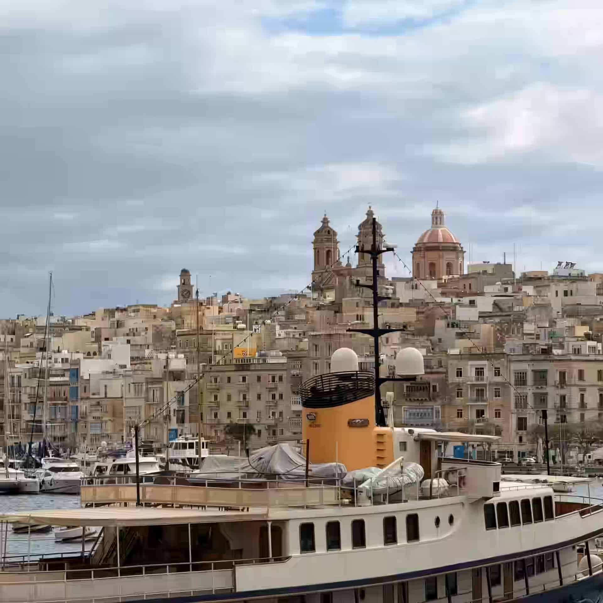 Eine große Yacht in der Marina von Birgu, Malta, unterhalb der terrassenförmigen Steinhäuser und der Kuppelkirche der Three Cities.