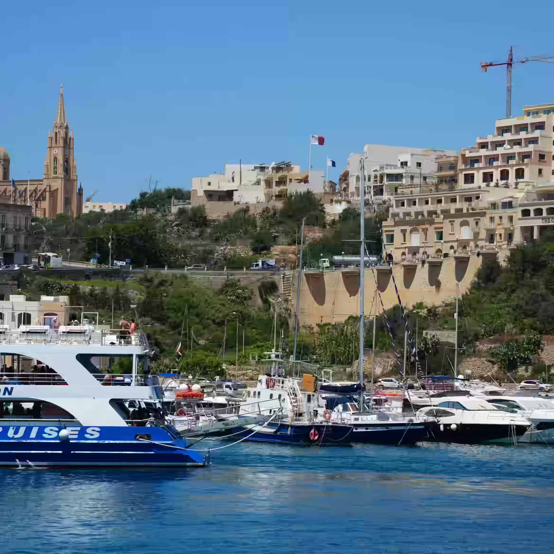 Der Hafen von Mġarr auf Gozo, Malta, mit Fähranleger, Fischerbooten und der Kirche am Hang darüber.