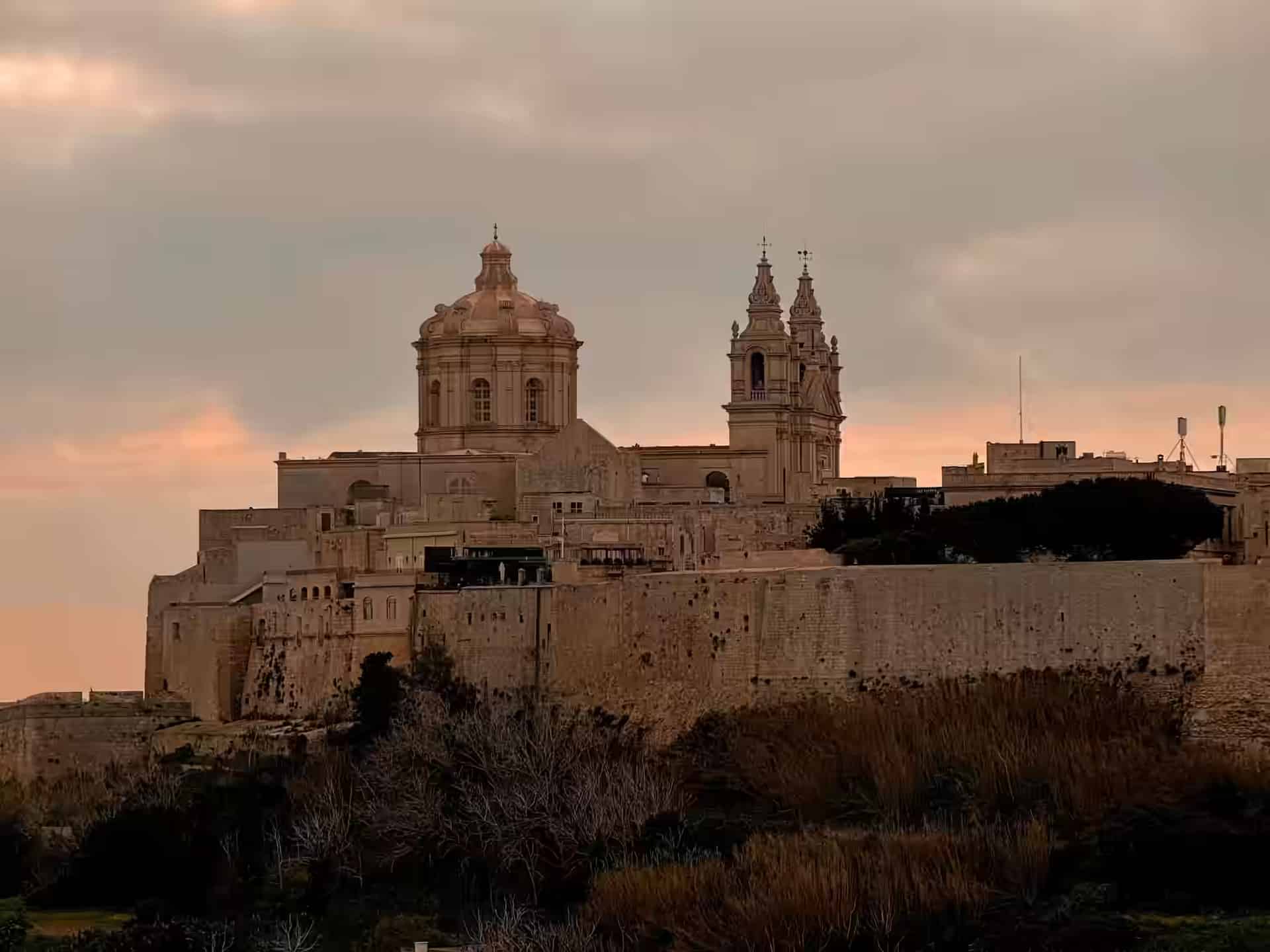 Kuppel und Glockentürme der St.-Pauls-Kathedrale über den Bastionsmauern von Mdina, Malta, in der Dämmerung.