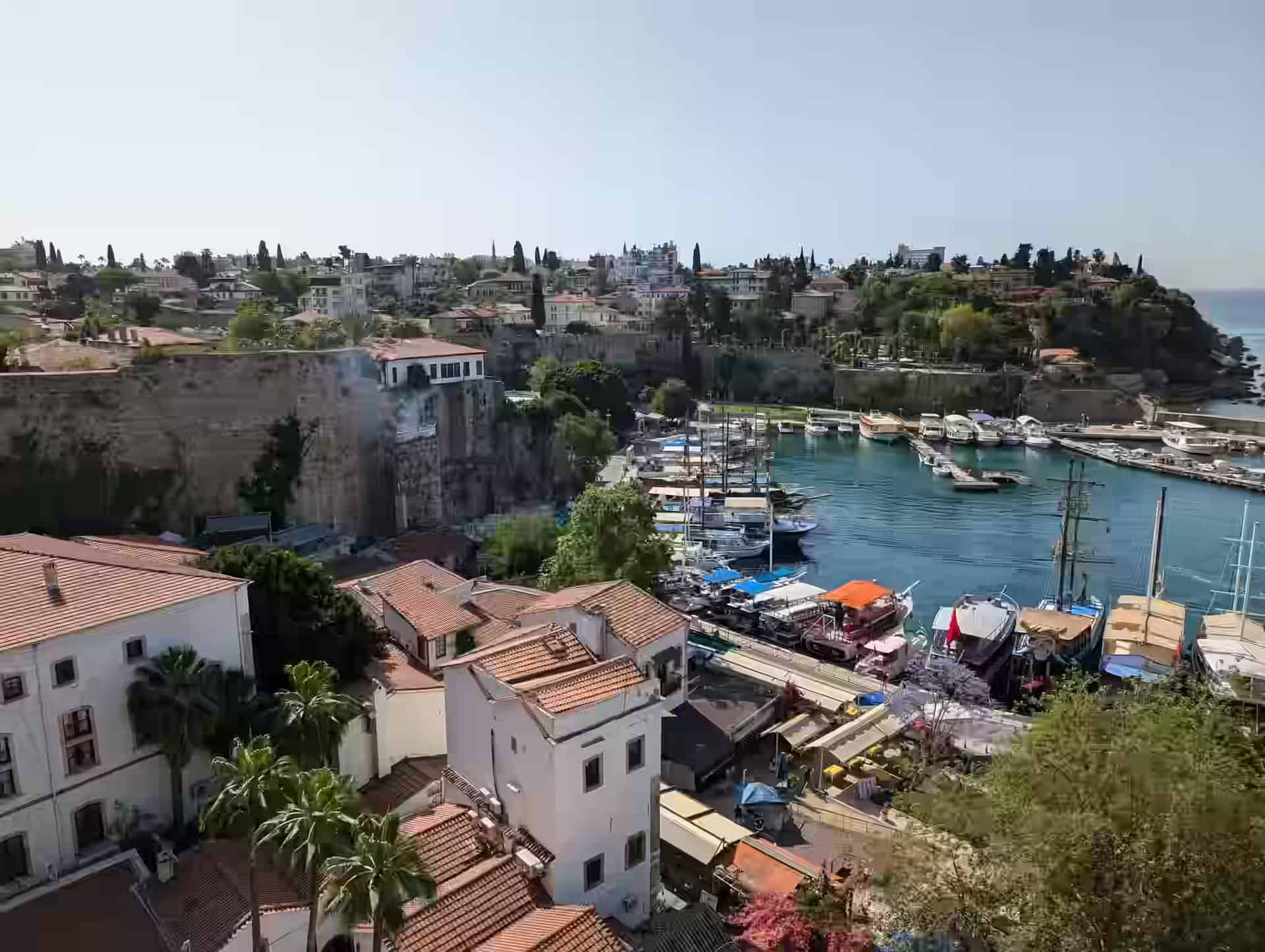 Red-roofed houses and stone walls around the boat-filled old harbour of Antalya, seen from above