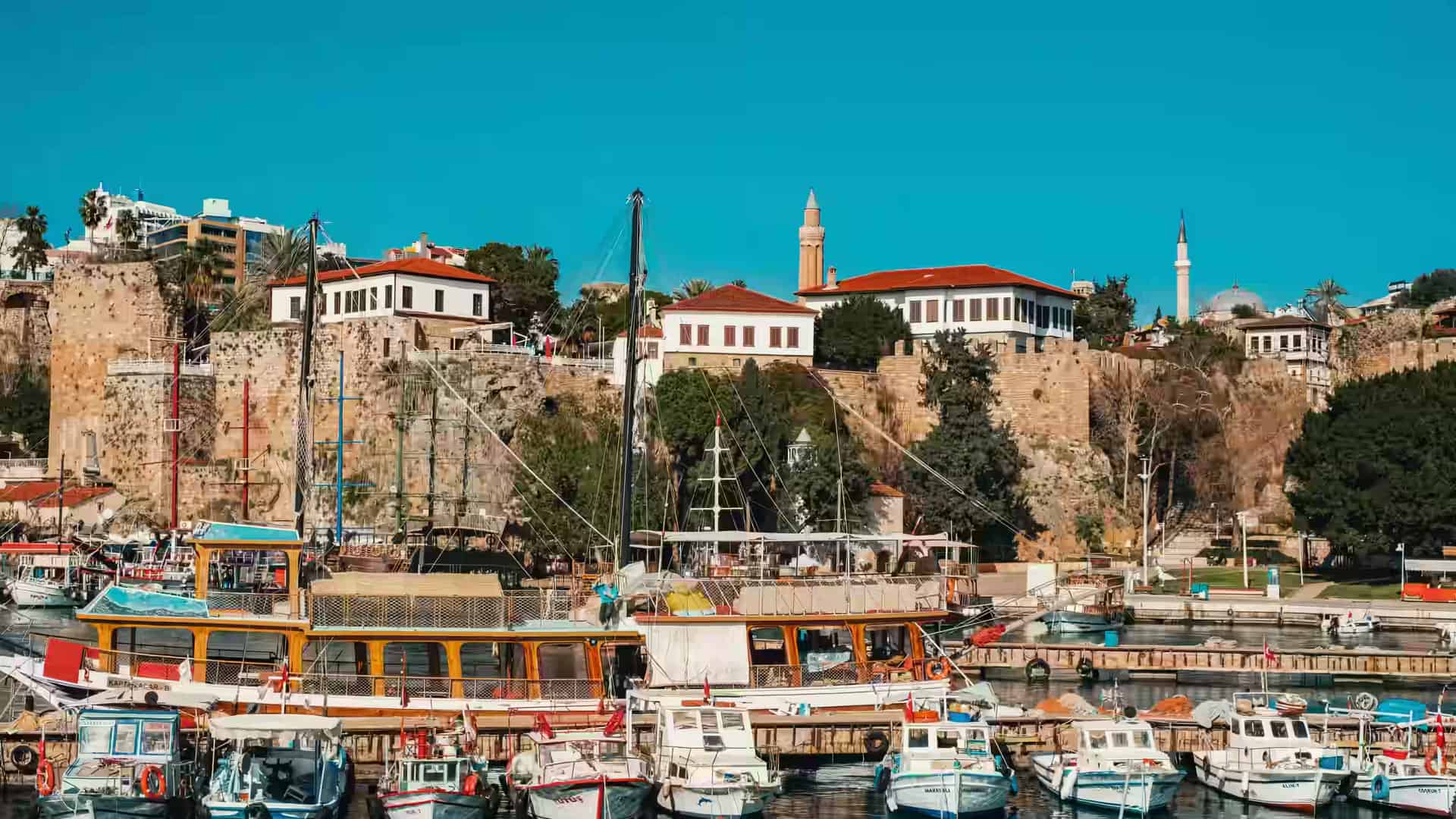Wooden boats moored in the old marina beneath the historic stone walls and minarets of Kaleiçi in Antalya