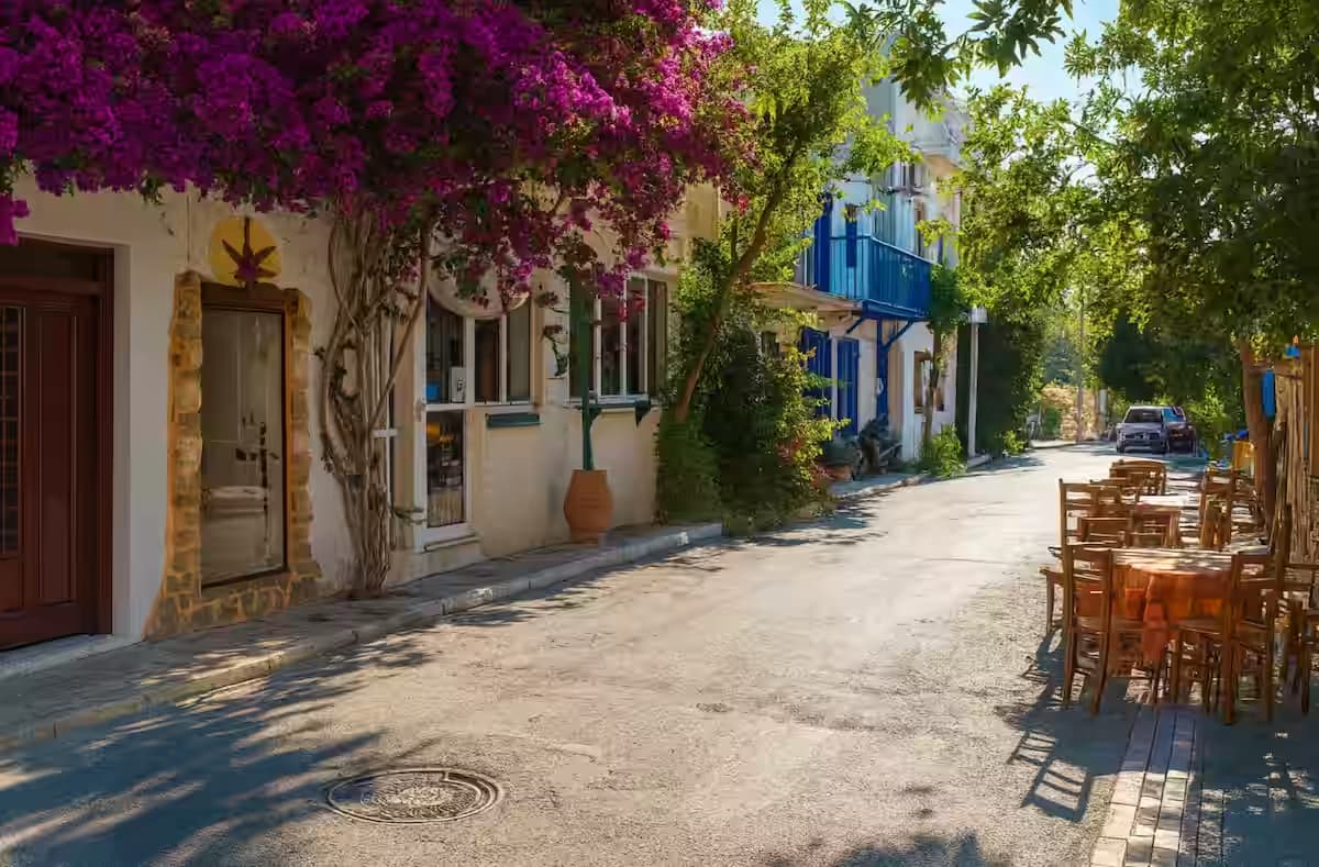 Παραδοσιακό δρομάκι στο χωριό Μύρτος, Ιεράπετρα, με ασβεστωμένα σπίτια, στενό πλακόστρωτο και έντονη ροζ βουκαμβίλια σε γαλάζιο ουρανό