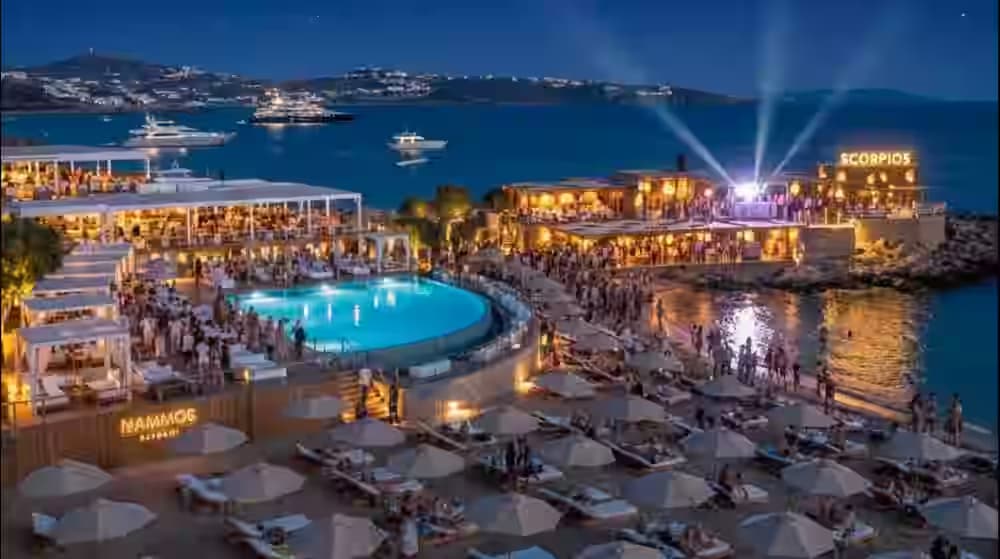 Vista aerea notturna di un lussuoso beach club di Mykonos con piscina illuminata e yacht ancorati