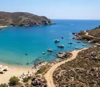 Vista aerea della baia di Panormos a Mykonos che mostra il contrasto tra lettini di lusso e natura selvaggia