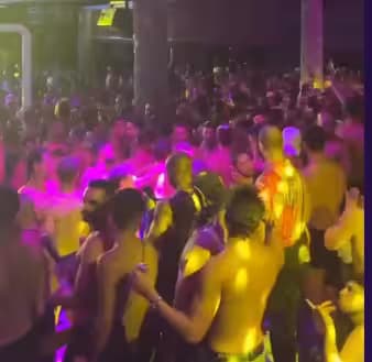 Grande folla che balla sotto luci vivaci rosa e gialle al festival XLSIOR di Mykonos