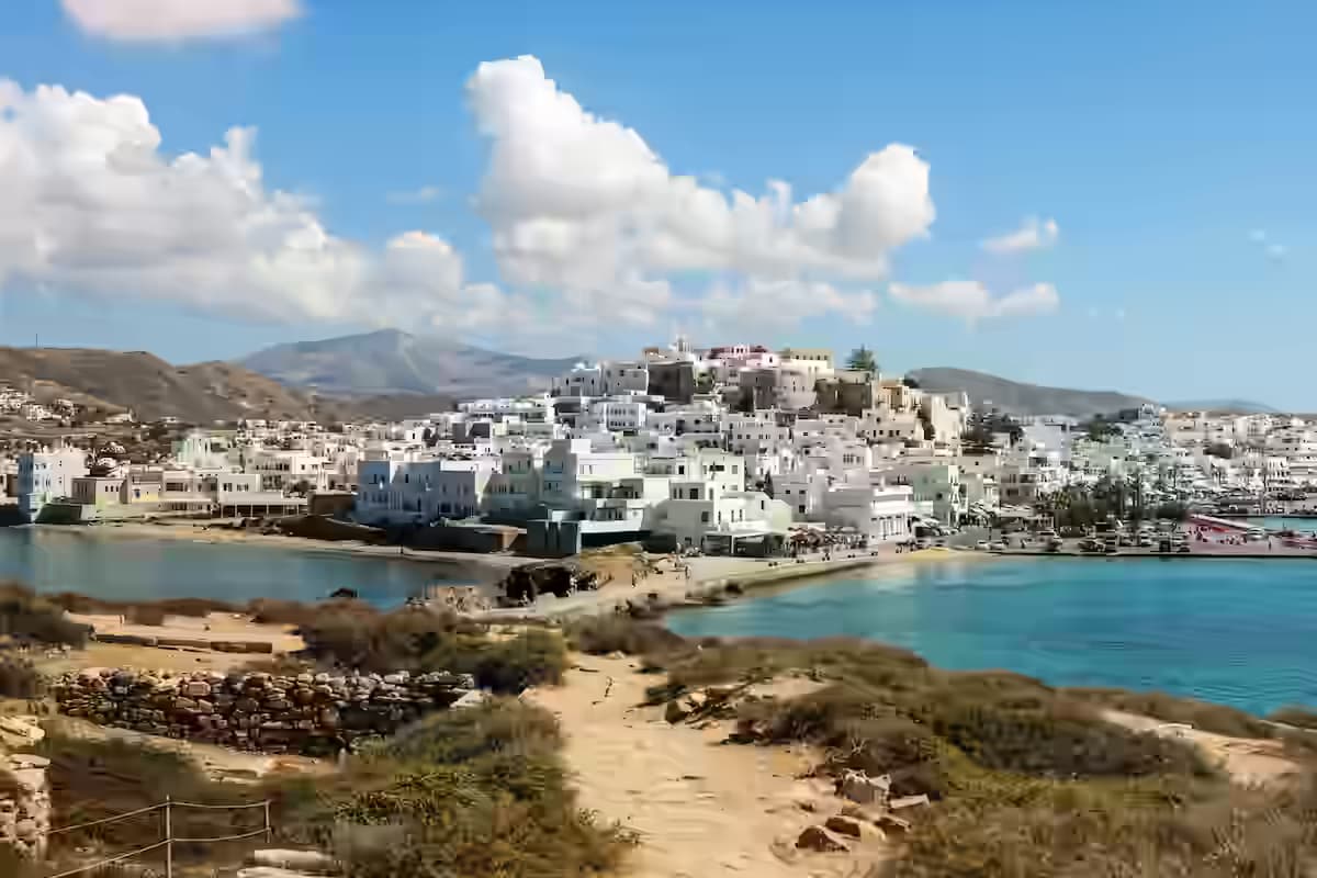 Panoramic daytime view of Naxos Town (Chora) featuring traditional whitewashed buildings, the harbor, and the connecting causeway, viewed from the islet of Palatia, Cyclades, Greece