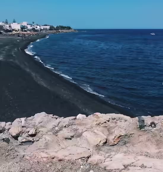 Perissa black-sand beach on Santorini's south coast with the dramatic profile of Mesa Vouno rock in the background