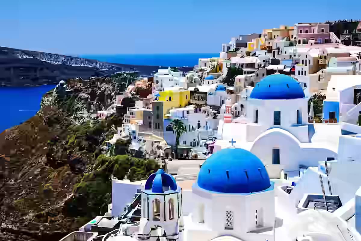 Panoramic view of Oia village on Santorini's caldera rim with whitewashed cubic houses, blue-domed churches and the deep-blue Aegean Sea below