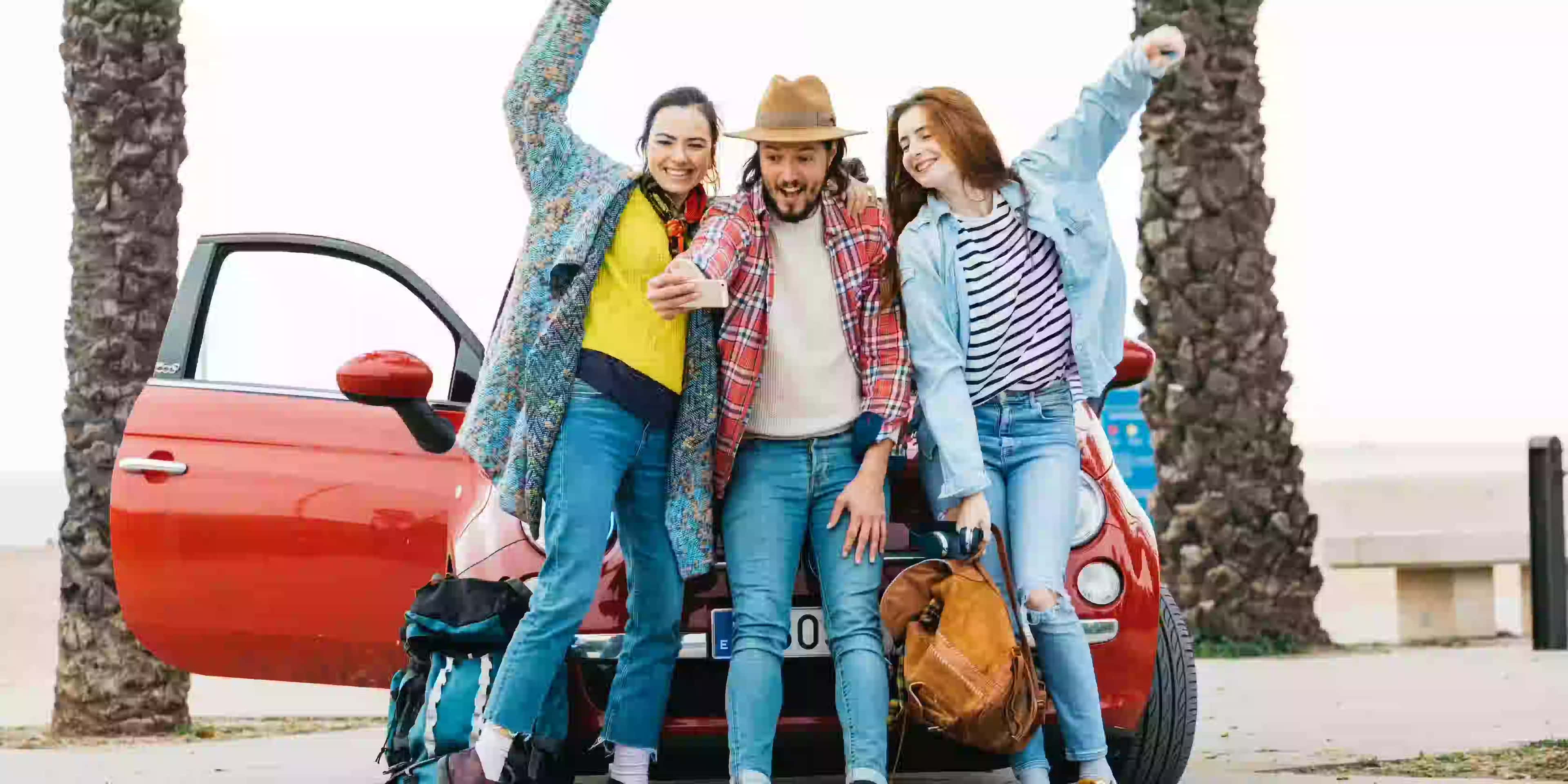 Young adults cheering with their rented vehicle, symbolizing the excitement of starting a new journey.