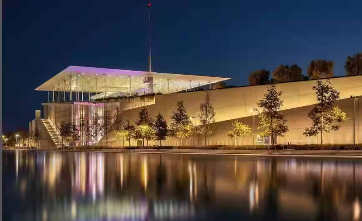 Modern illuminated building of the Stavros Niarchos Foundation Cultural Center at night reflected in the water canal, a top Athens attraction to visit by rental car.