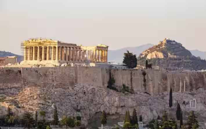 Aerial sunset view of the Acropolis hill and the Parthenon overlooking the historic Plaka district in Athens, a must-see landmark for travelers exploring Greece by rental car
