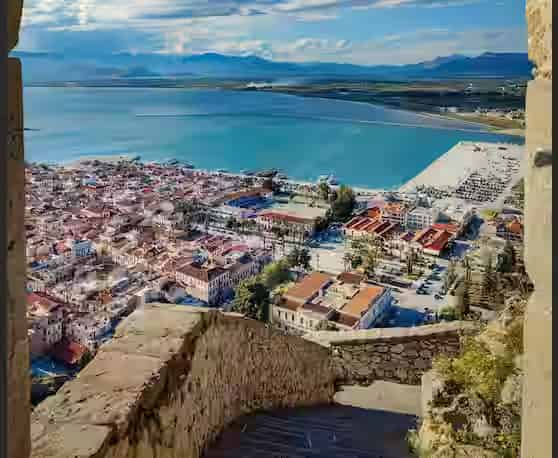 View of Nafplio town and the Argolic Gulf through a stone archway at Palamidi Castle, a top road trip destination for car rentals starting from Athens.