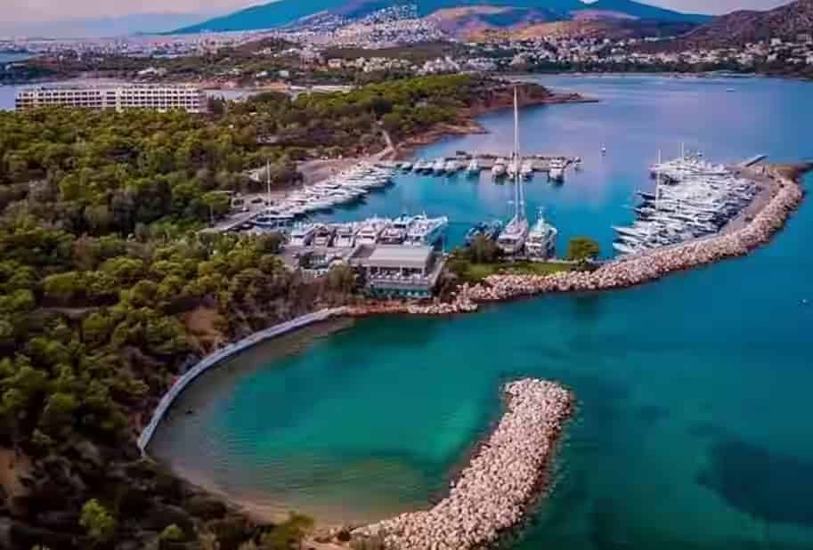 Aerial view of the luxury Vouliagmeni Marina and the lush Astir Peninsula in Athens Riviera, a perfect summer road trip destination for car rental travelers.