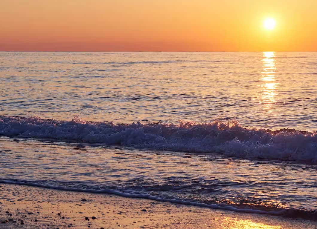 Couleurs dorées du coucher de soleil se reflétant sur la Méditerranée tandis qu’une vague se brise sur une plage de sable en Crète