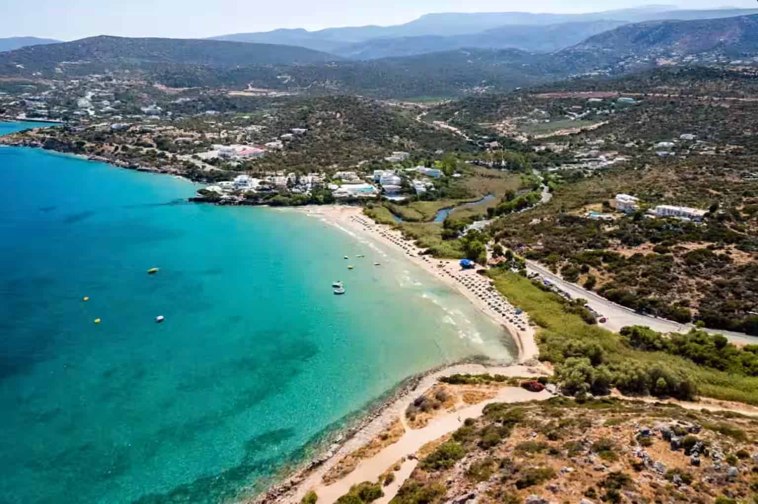 Εναέρια θέα της παραλίας Αλμυρός με τιρκουάζ νερά, ρέμα που εκβάλλει στη θάλασσα και resort ζώνη στο Ηράκλειο, Κρήτη