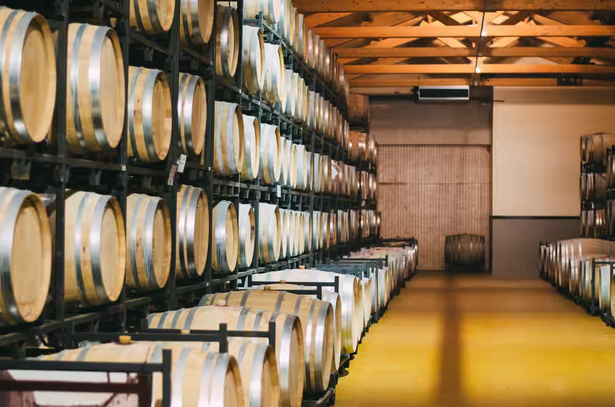 Rows of stacked oak wine barrels aging red or white wine inside a Cretan winery cellar
