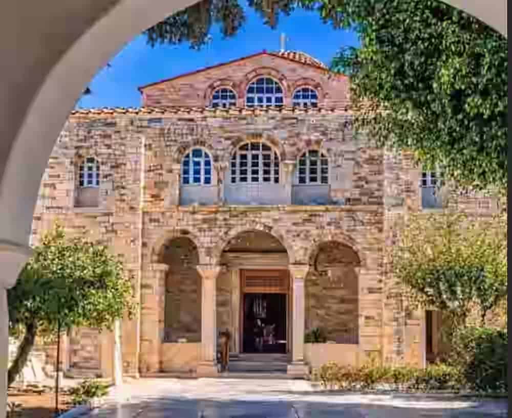 La storica facciata in pietra della chiesa bizantina Panagia Ekatontapiliani a Parikia, Paros, incorniciata da un arco tradizionale. Una tappa imperdibile durante la visita dell'isola con un noleggio auto Karpadu.