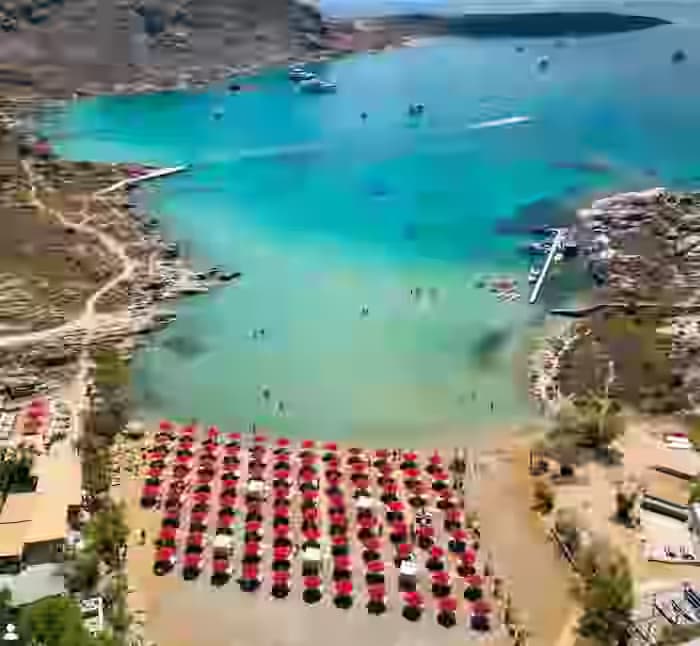 Luftaufnahme des Monastiri Beach auf Paros, Griechenland, mit organisierten Liegen, einer ruhigen türkisblauen Bucht und der felsigen Umgebung des Paros Parks. Genießen Sie erstklassige Inselmobilität mit einem Karpadu Mietwagen.