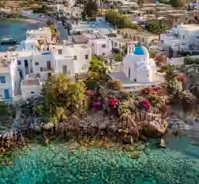 Aerial view of Piso Livadi harbor in Paros, Greece, featuring the blue-domed Agios Nikolaos church overlooking the Aegean Sea. A charming seaside village best explored with a Karpadu car rental