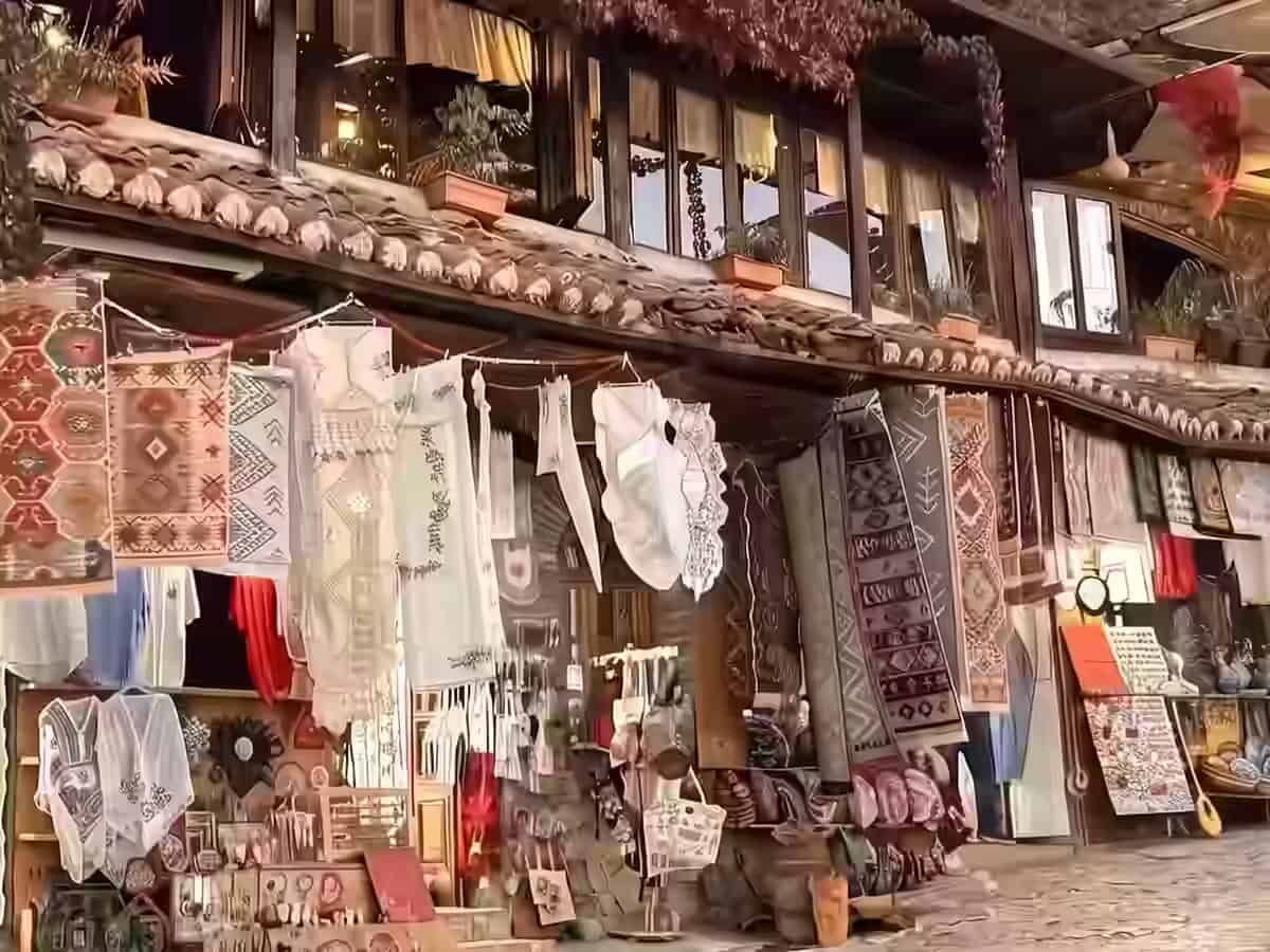 Covoare și țesături tradiționale atârnate în fața unei prăvălii de lemn pe strada pavată a vechiului bazar din Kruja, Albania.