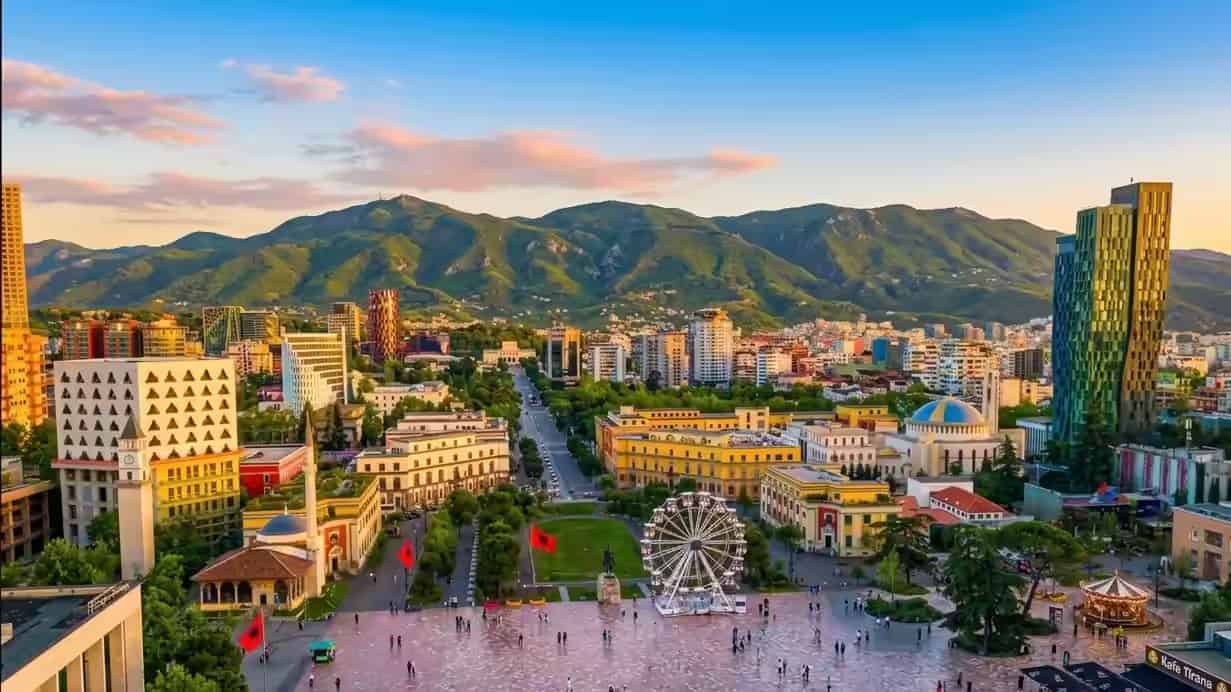 Verhoogd uitzicht op het Skanderbegplein en de skyline van Tirana, Albanië, met de bergen op de achtergrond bij zonsondergang.