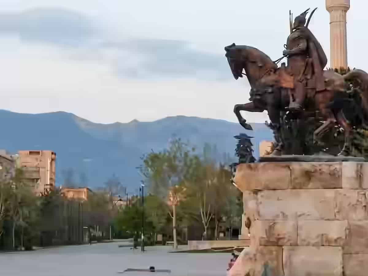 Monumentul din bronz al lui Skanderbeg pe un piedestal de piatră, în Piața Skanderbeg din Tirana, Albania, cu munții în fundal.
