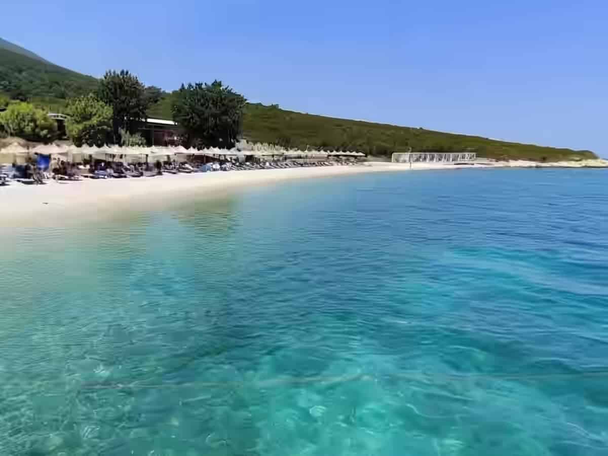 Klares blaues Wasser und ein Kiesstrand mit Liegen und Sonnenschirmen im Meerespark Karaburun-Sazan, Albanien.