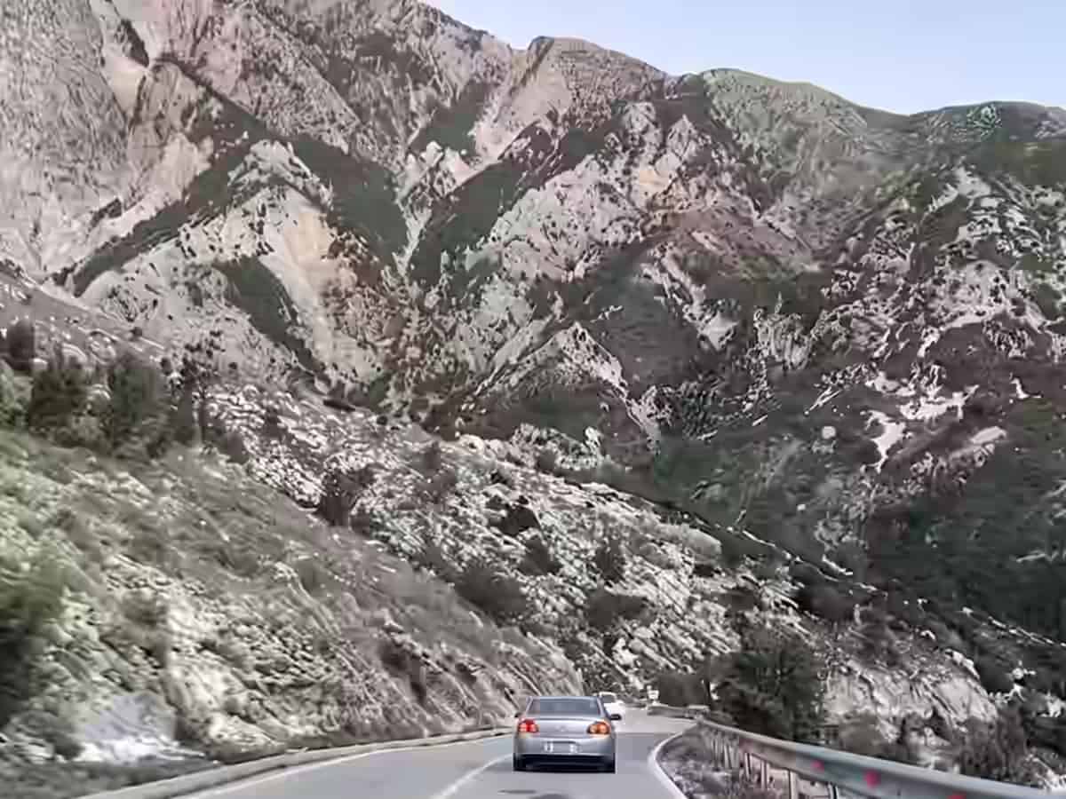Ein silbernes Auto auf der kurvenreichen Passstraße des Llogara-Passes in Albanien, umgeben von steilen Felshängen.
