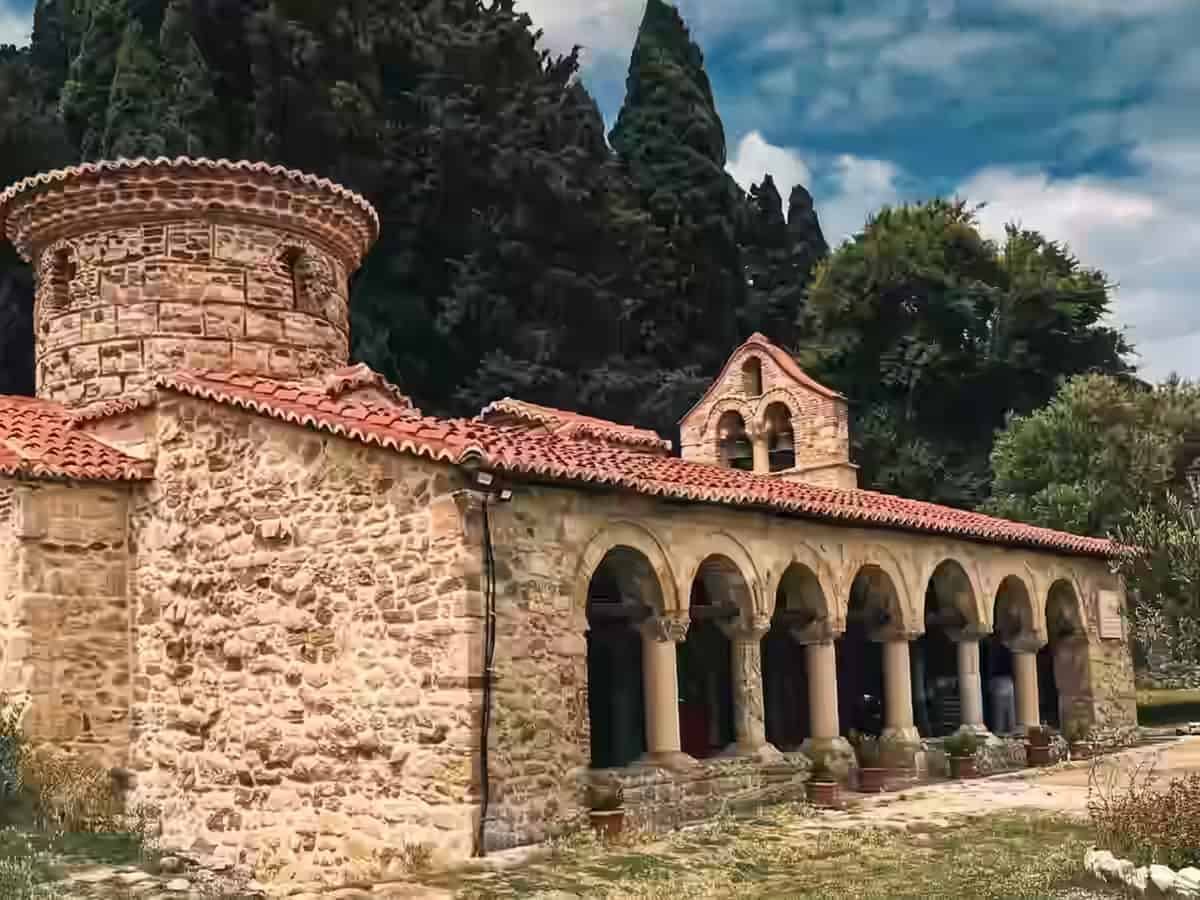 Die alte Steinarchitektur und die Bogengänge des Klosters Zvërnec, umgeben von hohen grünen Zypressen, in Albanien.