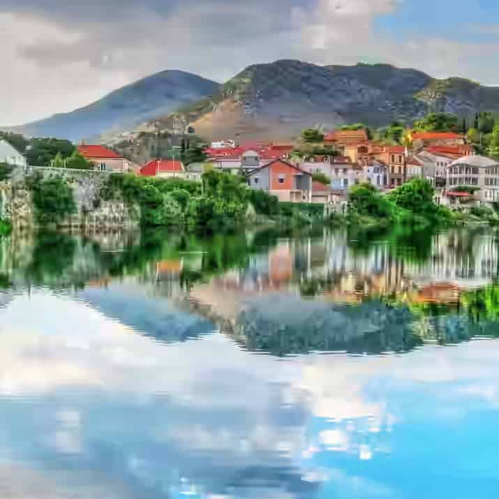 Mirna reka u kojoj se ogledaju kuće sa crvenim krovovima i kameni most grada Trebinja, Bosna i Hercegovina.