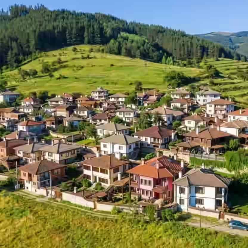 Traditionelle Häuser mit roten Ziegeldächern dicht beieinander im grünen Bergtal von Kopriwschtiza, Bulgarien.