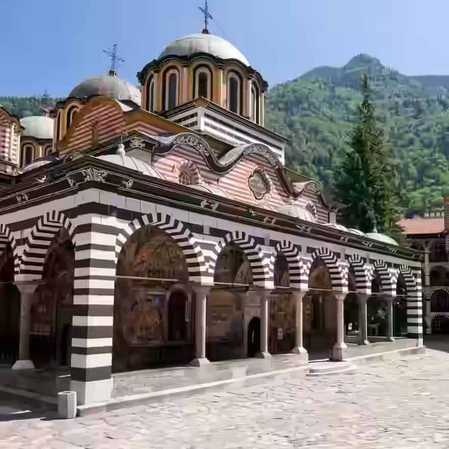 Die schwarz-weiß gestreiften Steinbögen und Kuppeln des Rila-Klosters vor einem grünen Berg, Bulgarien.
