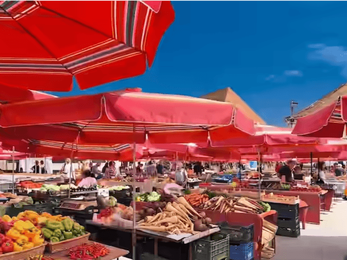 Leuchtend rote Sonnenschirme über den Ständen mit frischem Obst und Gemüse auf dem Dolac-Markt in Zagreb, Kroatien.