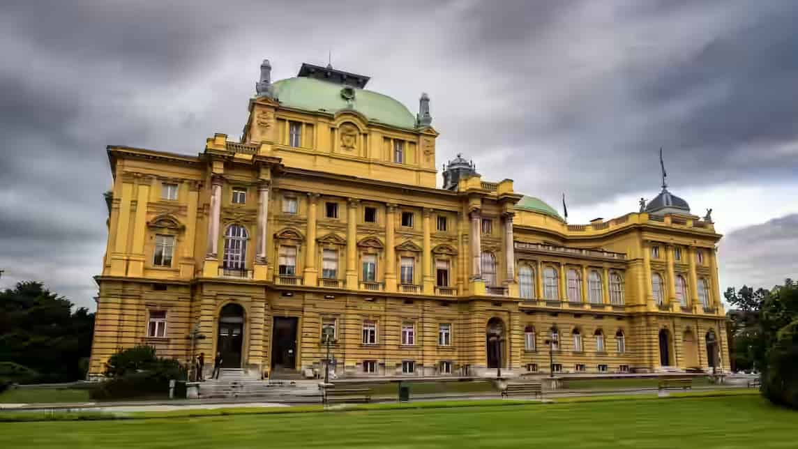 The yellow neo-baroque façade and green domes of the Croatian National Theatre in Zagreb, Croatia.