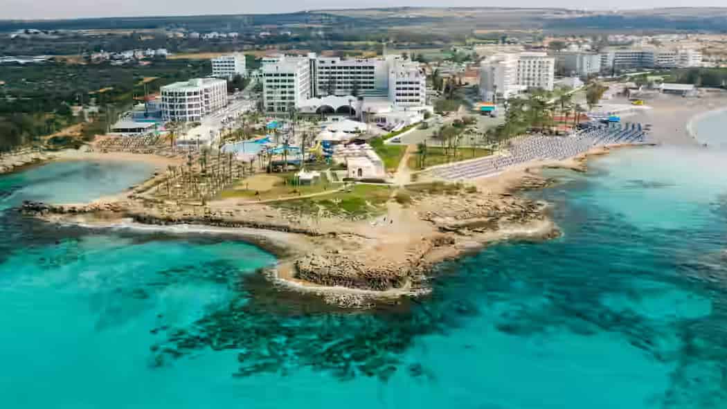 Hotels aan de kust, zwembaden en een zandstrand op een rotsachtig schiereiland aan de turquoise Middellandse Zee bij Paphos, Cyprus.