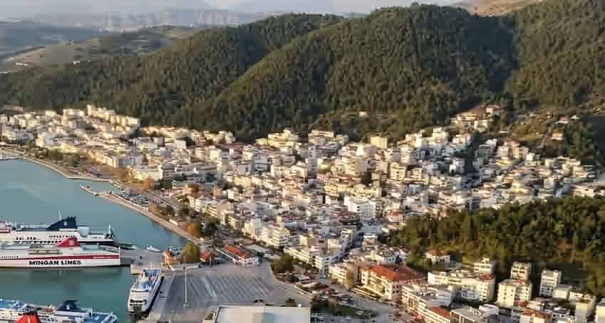 Vue aérienne du vieux port et du paysage urbain d'Igoumenitsa, Grèce, avec des ferries passagers amarrés, des bâtiments blancs et des collines boisées.