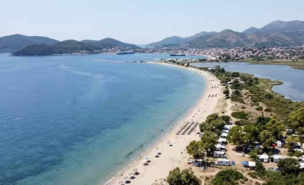 Vue aérienne de la plage de Drepano à Igoumenitsa, Grèce, montrant une longue péninsule sablonneuse séparant la mer et la lagune, avec un camping boisé.