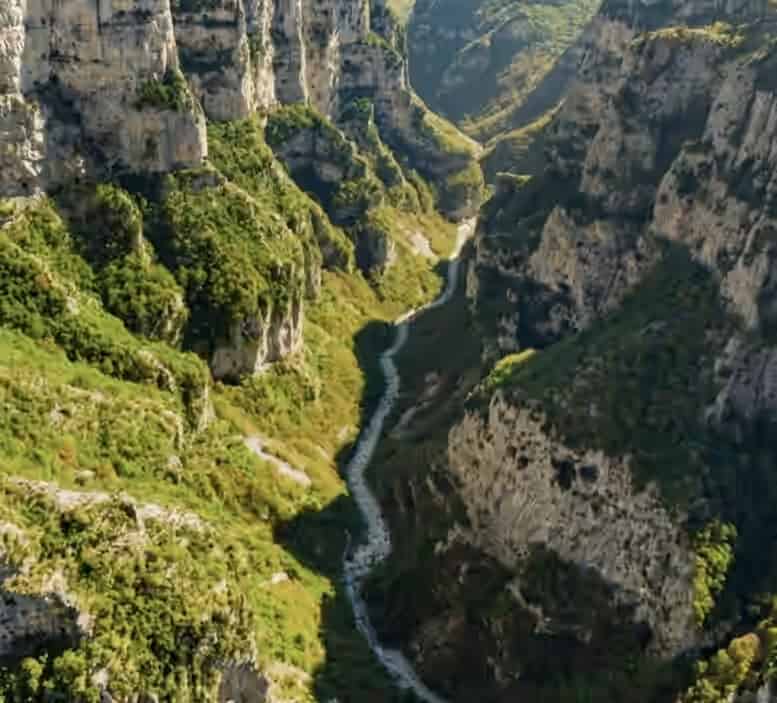 Vue aérienne des profondes parois rocheuses et de la végétation verte des gorges de Vikos en Grèce, avec une rivière sinueuse au fond de la vallée.