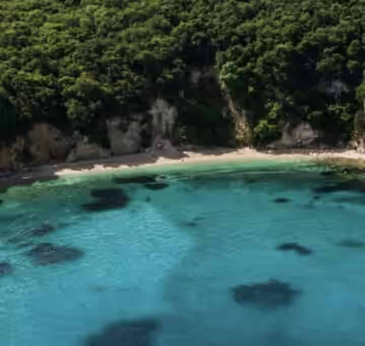 Eau turquoise claire et petite crique sablonneuse du Blue Lagoon à Vraka, Grèce, entourée de falaises rocheuses et d'une forêt verte dense.