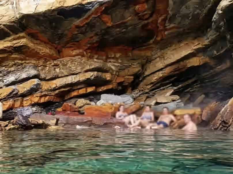 People relaxing in the natural thermal waters of Therma hot springs inside a rocky cave in Ikaria, Greece.