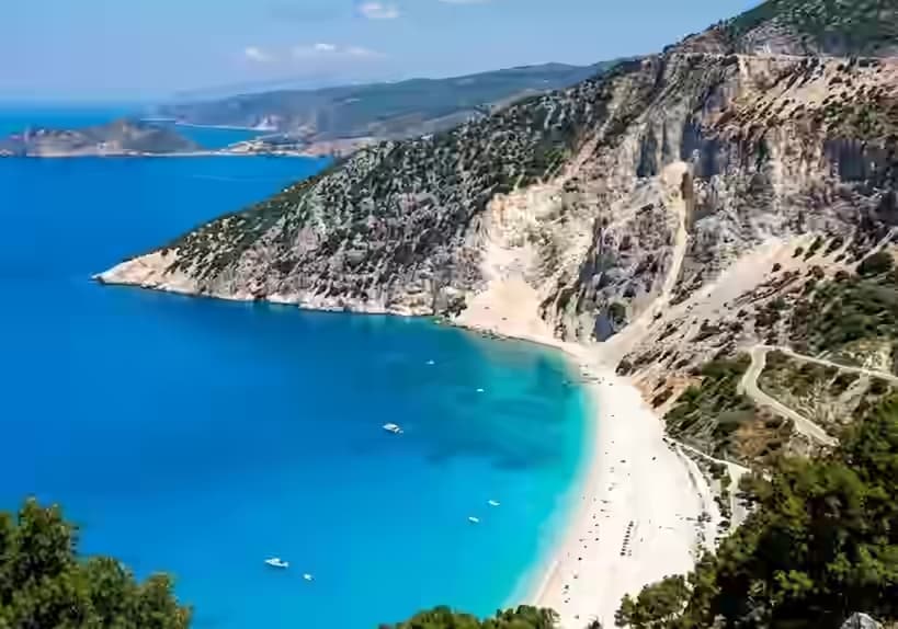 Vista aerea della spiaggia di Myrtos su Cefalonia con acqua blu elettrico, riva di ciottoli bianchi e falesie calcaree a picco, isole Ionie, Grecia