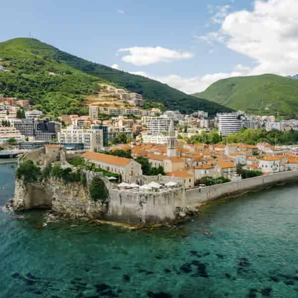 Scenic view of the medieval old town walls of Budva meeting the clear blue Adriatic Sea.