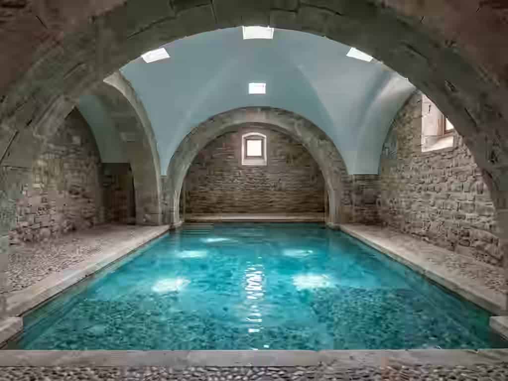 Vue intérieure des bains thermaux curatifs traditionnels, avec un bassin paisible d'eau turquoise cristalline entouré de murs rustiques historiques en pierre, d'un sol pavé et d'arcs voûtés, à Lesbos, Grèce.