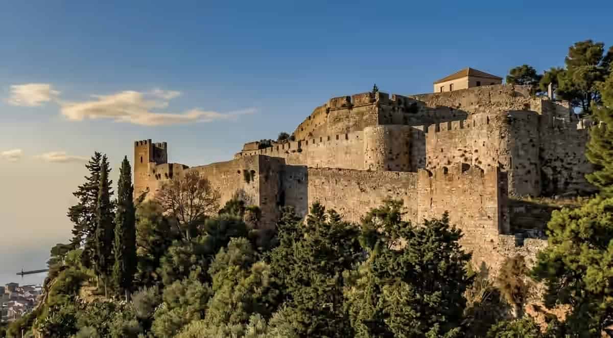 Stone walls and battlements of the medieval Vonitsa Castle on a tree-covered hill overlooking the town and water in Greece.