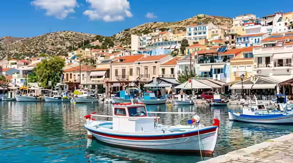 Traditional wooden fishing boats in the harbor of a coastal village in Samos, Greece, with colorful hillside buildings in the background.