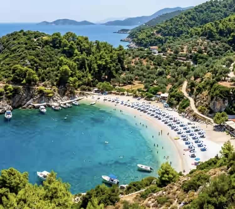 Aerial view of Lemonakia beach in Samos, Greece, showing a secluded cove with clear water, sun loungers, umbrellas, and small boats.